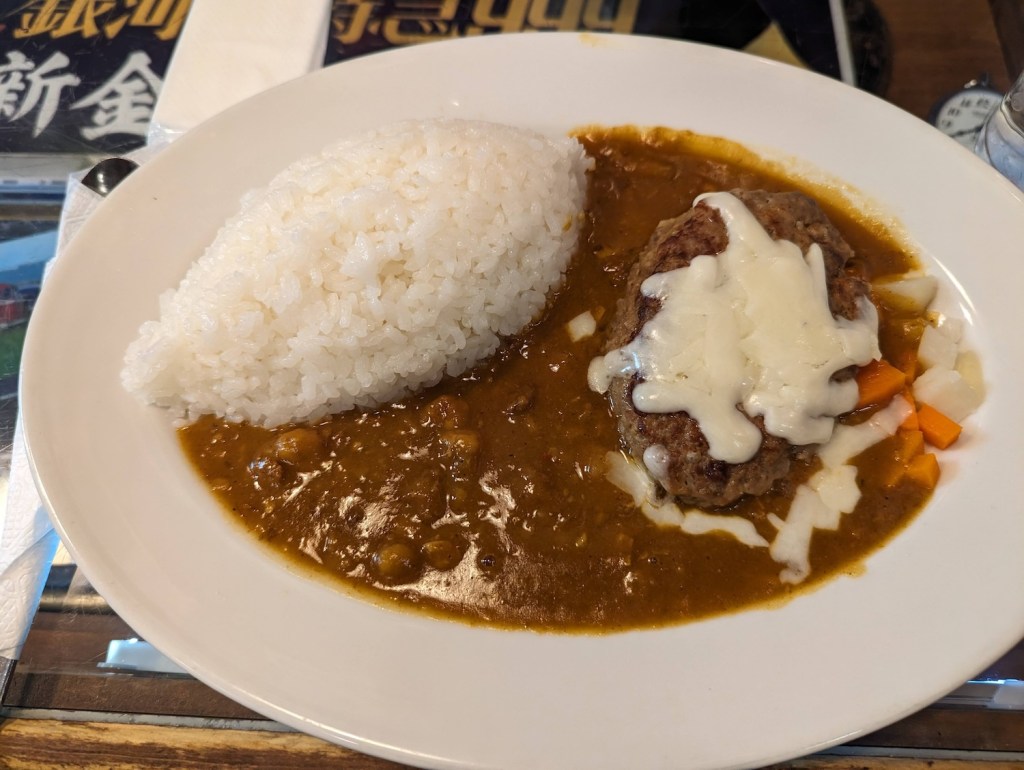 A plate of hamburg curry, with the rice in a football shape, cheese sauce on the hamburg steak, and plenty of curry sauce