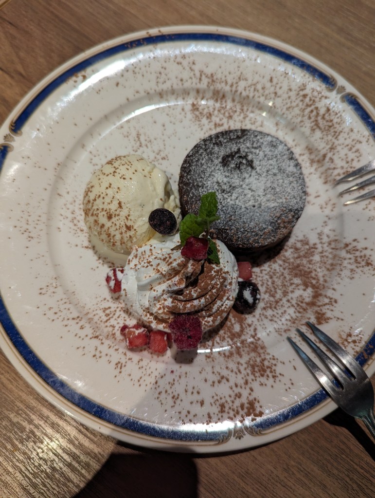 A plate with a small round cake, some vanilla ice cream, and some whipped cream