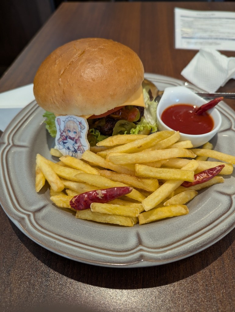 A burger, fries, and ketchup with a little edible Haachama wafer. There are dried peppers sprinkled sparingly over the dish.