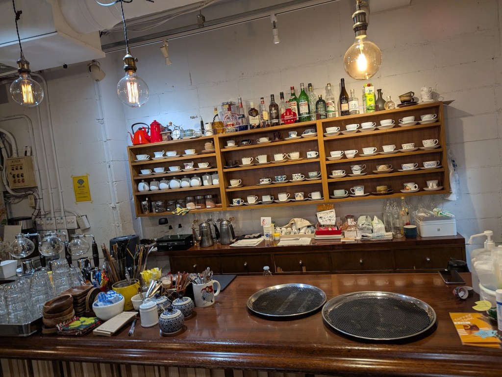 A coffee shop counter, with coffee cups on shelves in the back.