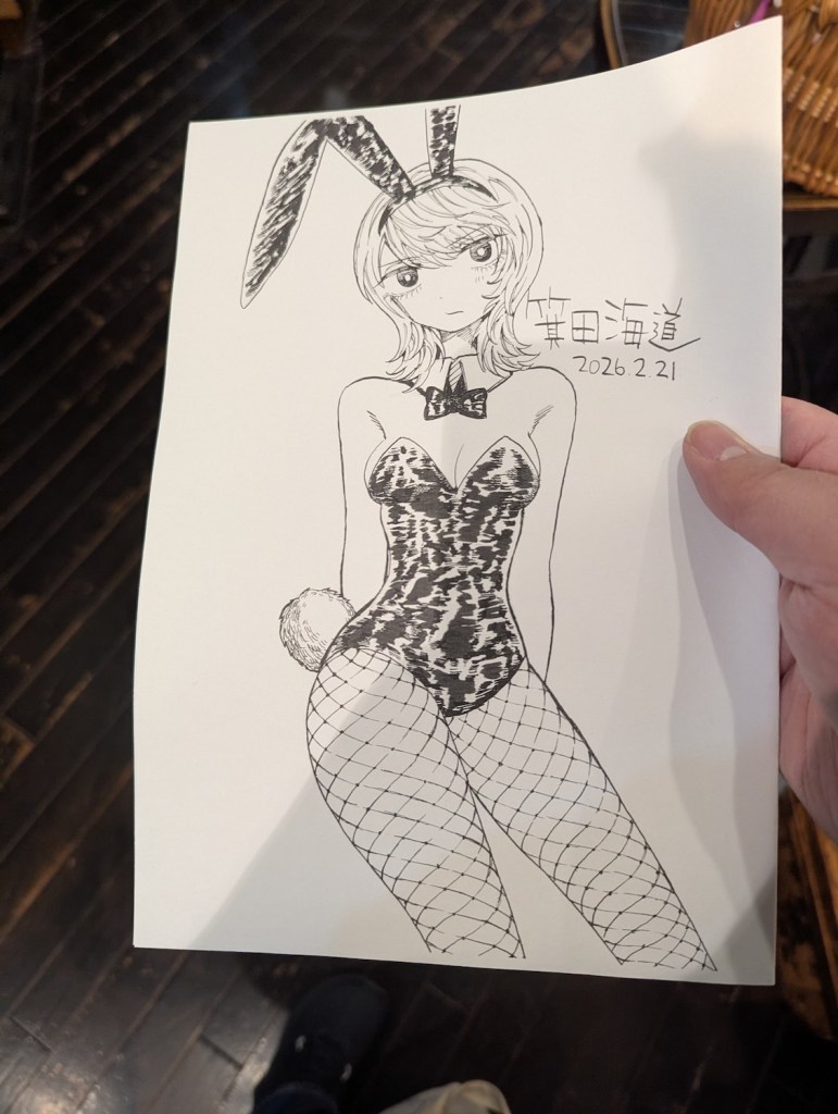 A hand holding a drawing of a bunny girl. The girl has a stoic look, medium-length hair, bangs, hands behind body, and medium breasts. It is signed "Minoda Kaidou."