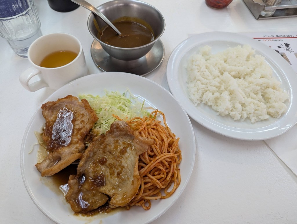 A cup of soup, bowl of Japanese curry, a plate of white rice, and a plate of ginger pork with ketchup spaghetti and cabbage.